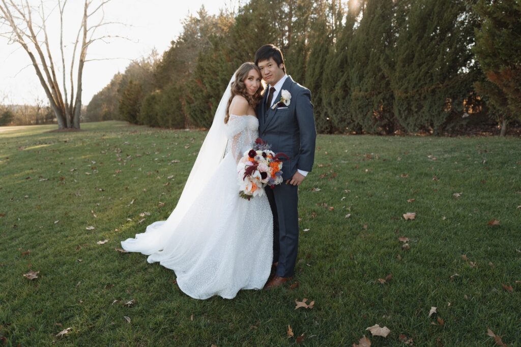 An image of a bride and groom at their chosen partially inclusive wedding venue. Bride is in a white sparkling dress holding a bouquet. Groom is in a three-piece navy suit. They are standing close together.