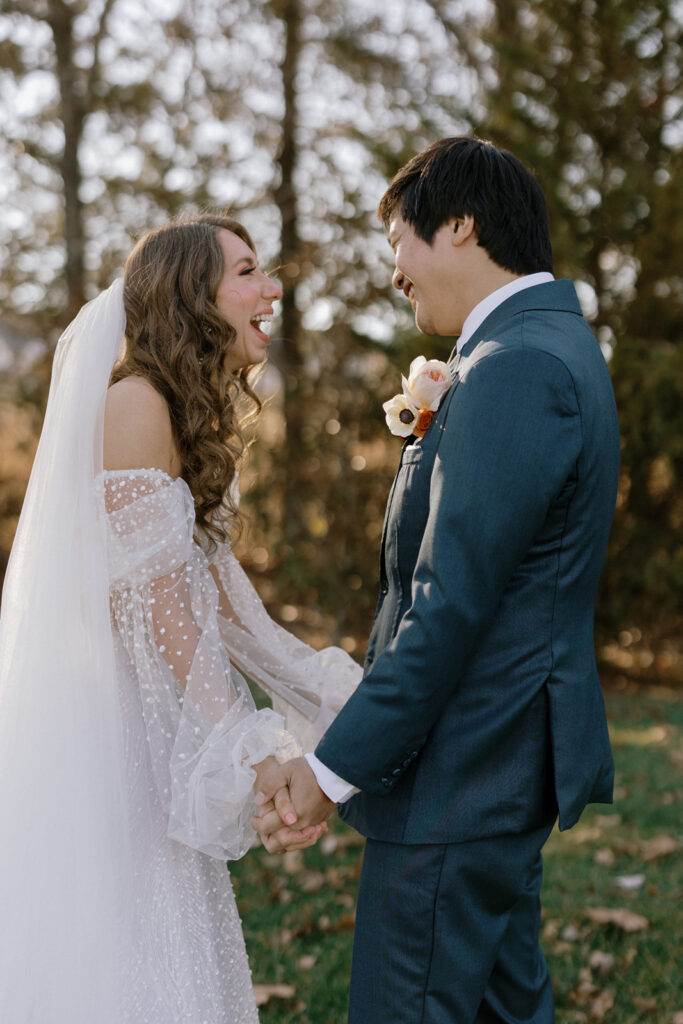 Bride and groom facing each other holding hands with huge smiles on their faces after revealing their wedding outfits.