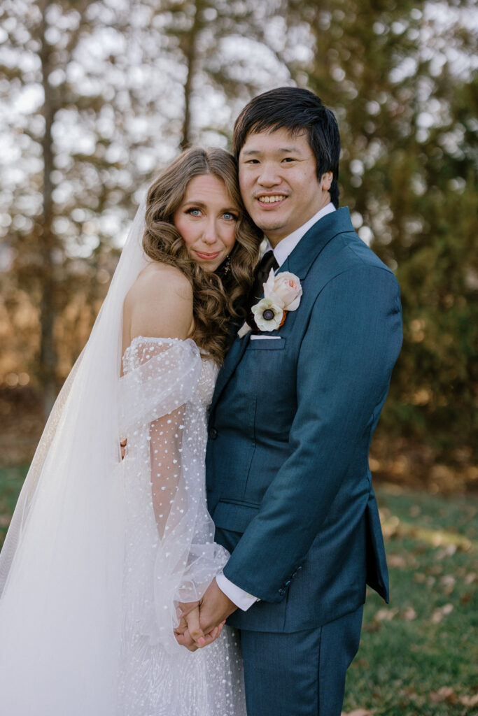 Bride and groom holding hands and leaning into each other while smiling into the camera before their wedding.