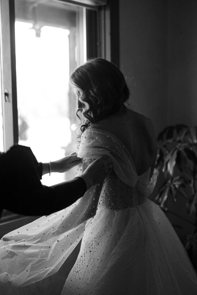 Bride being assisted in putting on her wedding dress sleeves. 