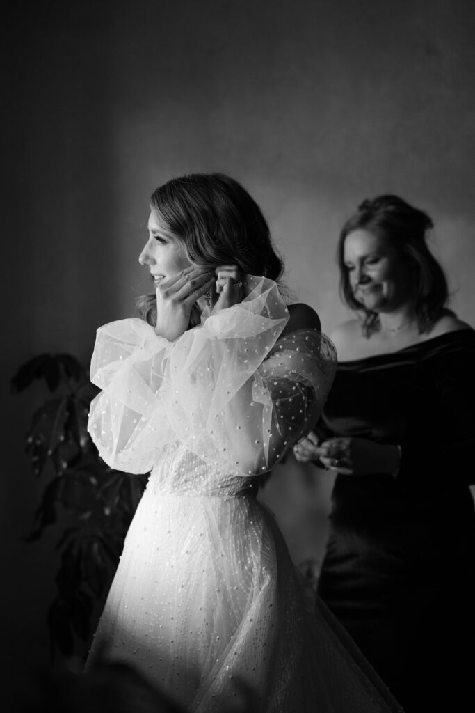 Bride in her custom wedding dress putting in earrings to finish her outfit.