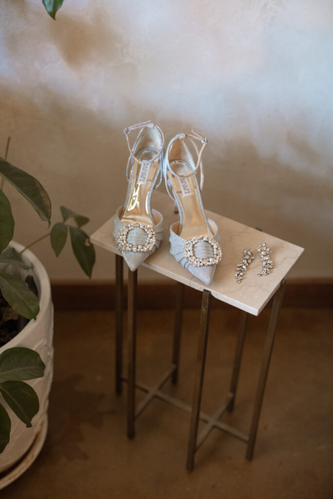 Light blue shoes of the bride set on a small table with crystal earrings laid beside. 