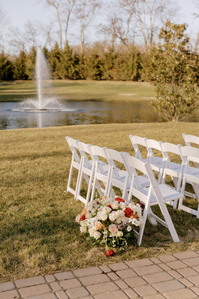 White folding chairs for the wedding ceremony with a large floral arrangement.