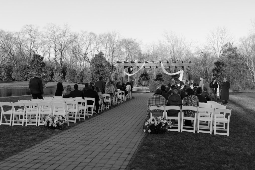 A black and white photo of guests seated in white folding chairs waiting for the wedding ceremony to begin.