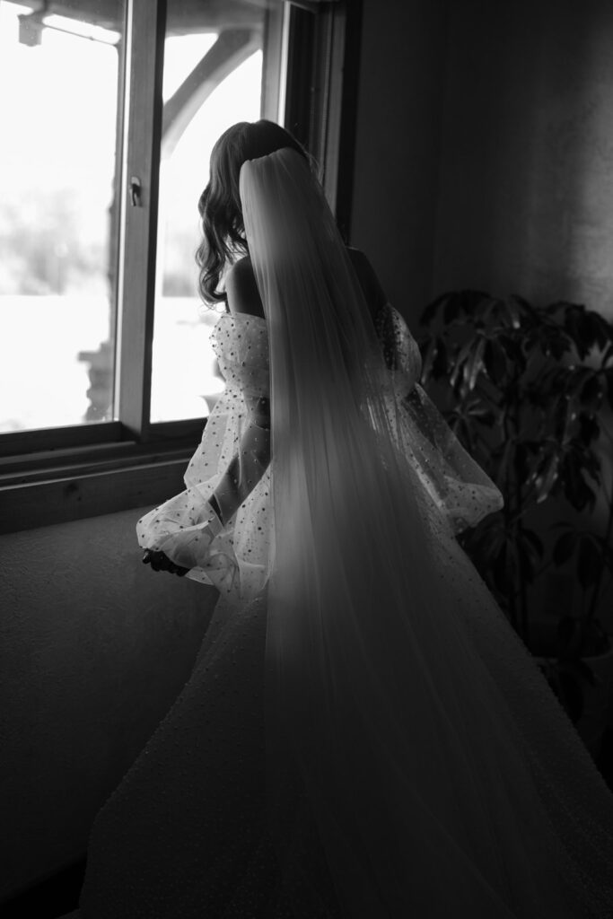 Bride in dress and veil peeking out the window of her bridal suite.