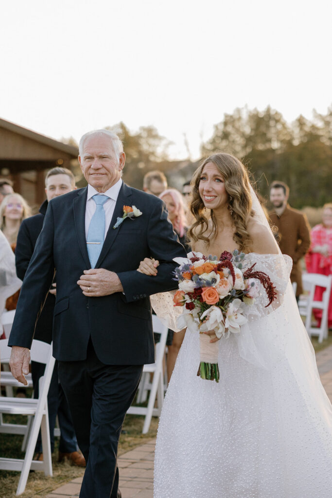 The bride smiling and crying with happiness as she walks down the aisle with her father.