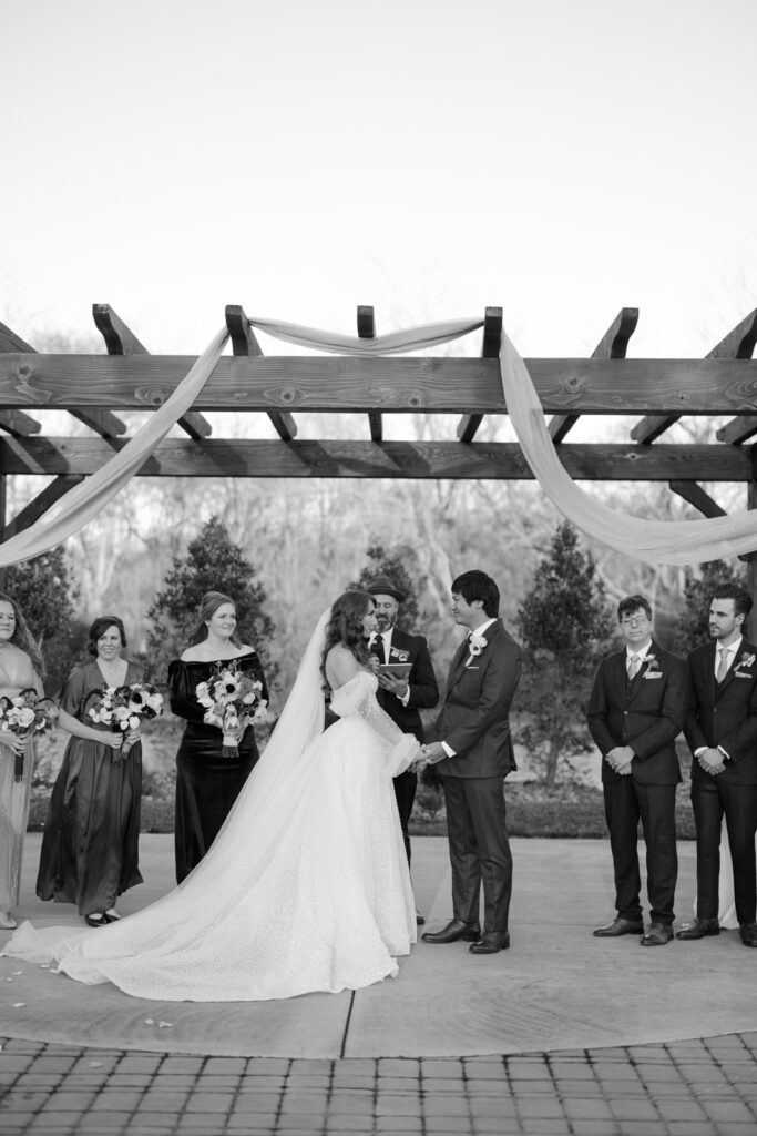 A black and white photo of the wedding ceremony where the couple is holding hands. 