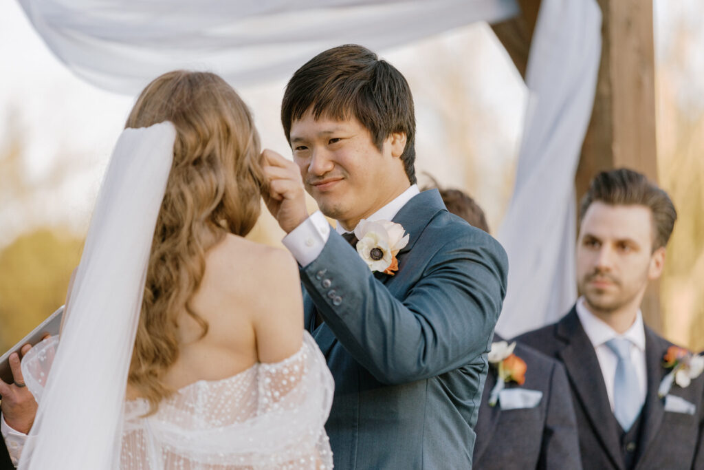 The groom at the altar wiping a tear from the cheek of the bride and smiling.