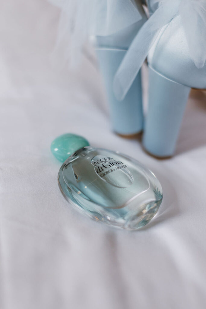 Blue wedding shoes and a bottle of Acqua di Gioia Armani perfume resting on a soft surface