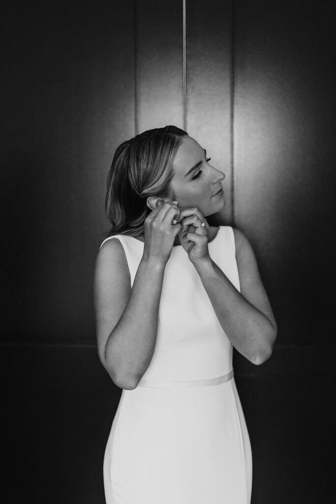 A bride in a white dress fastening her earrings