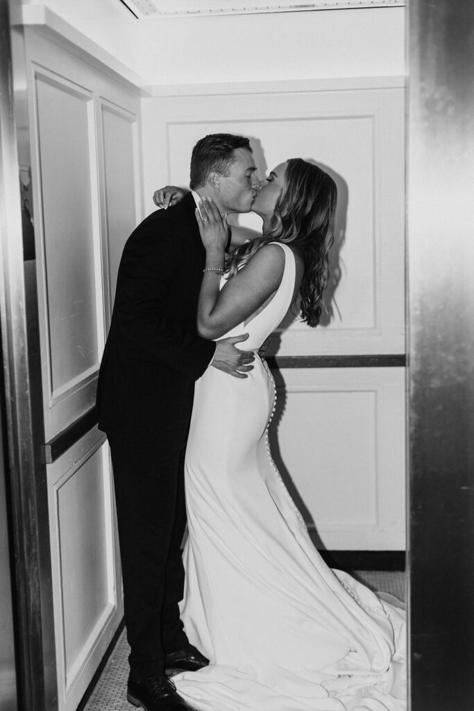 A bride and groom kiss passionately in a hotel elevator