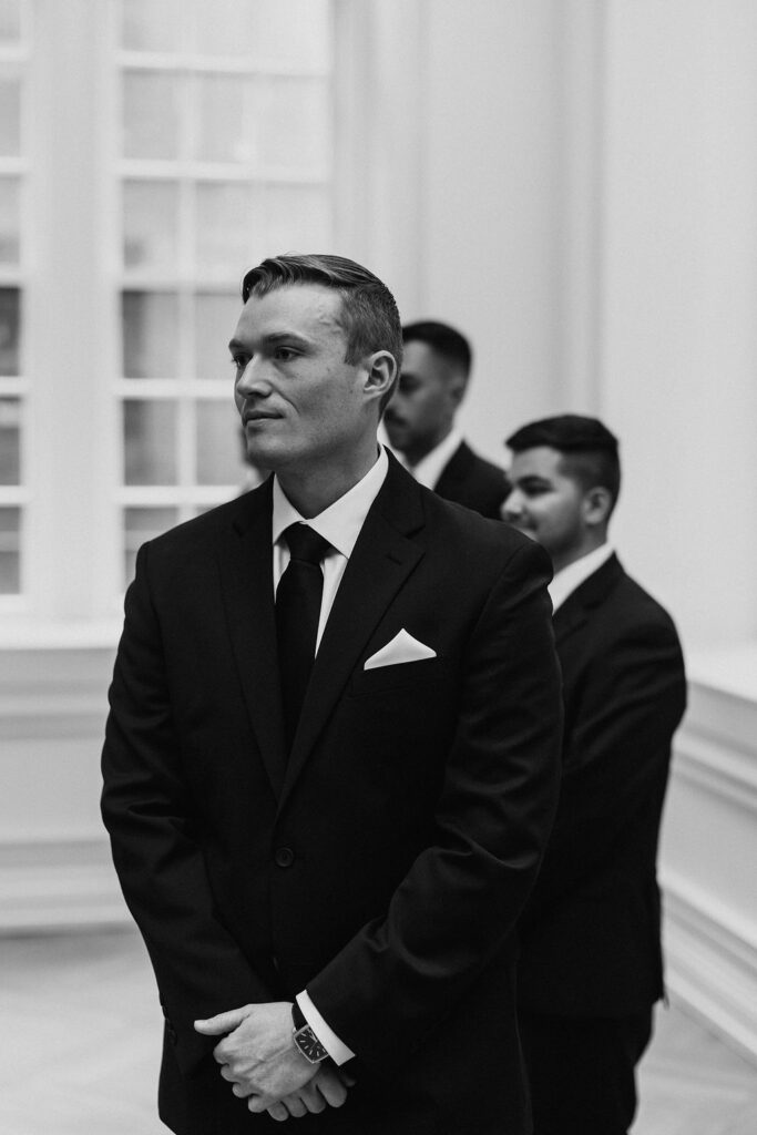 A groom in a black suit looks to the right