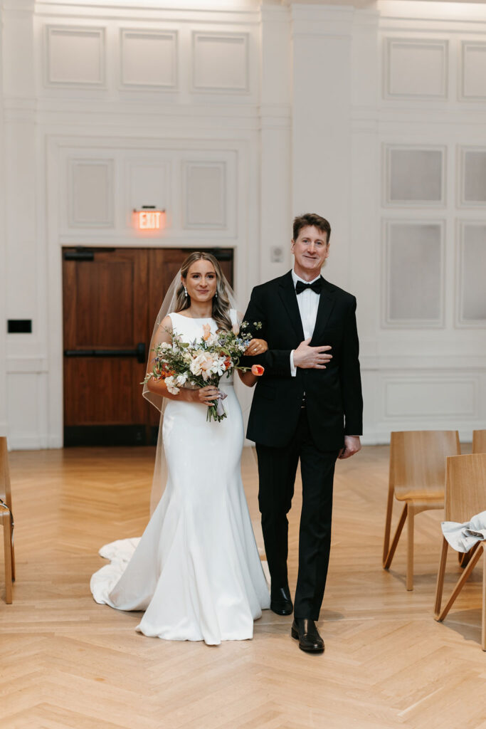 The bride and her father walk down the aisle as she carries a large colorful floral bouquet