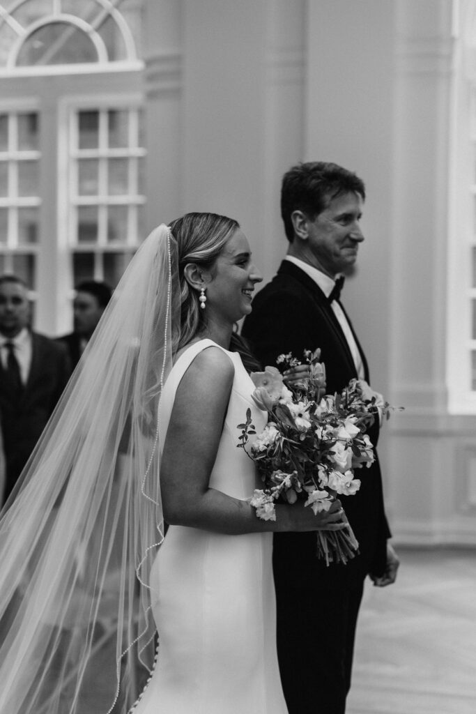 A bride and her father come to the end of the wedding ceremony and smile at the groom