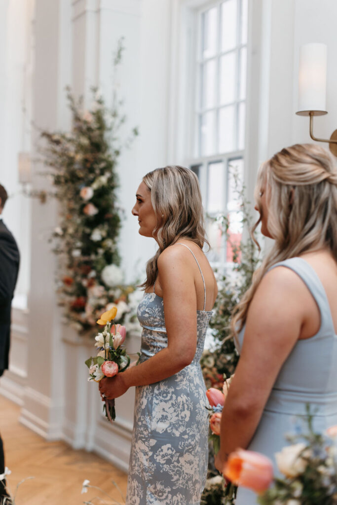 A side profile of two women in blue bridesmaid dresses holding colorful floral bridesmaid bouquets