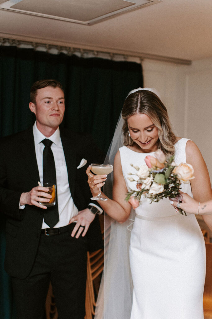 A groom looks happily at his bride as they drink cocktails