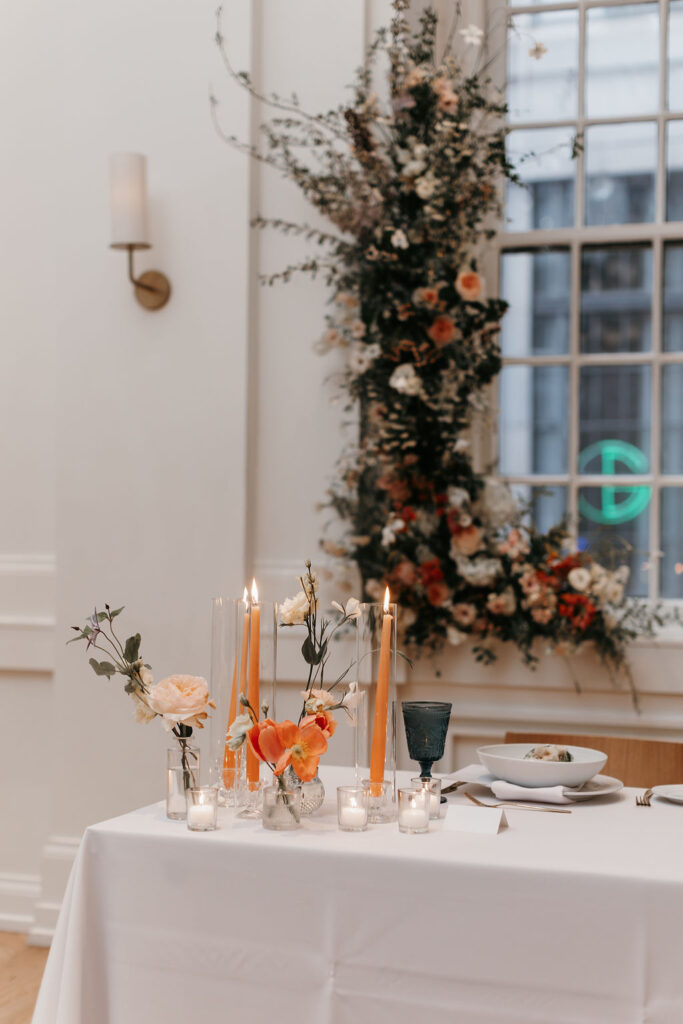 Wedding reception tables with orange taper candles and orange flowers set with blue water glasses and a caesar salad