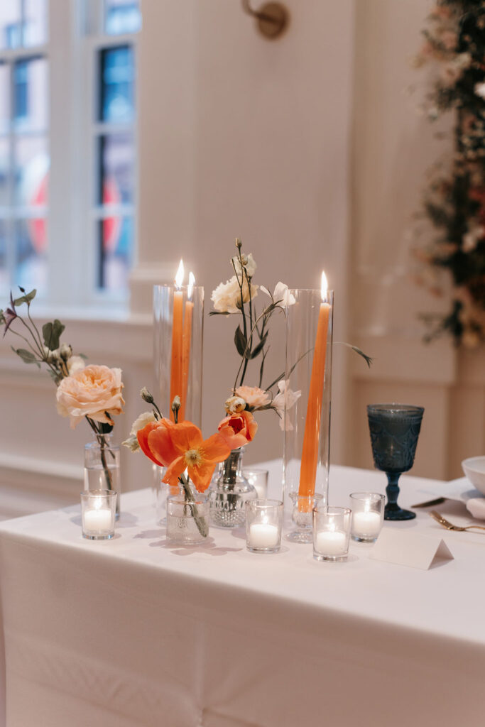 Wedding reception tables with orange taper candles and orange flowers set with blue water glasses and a caesar salad