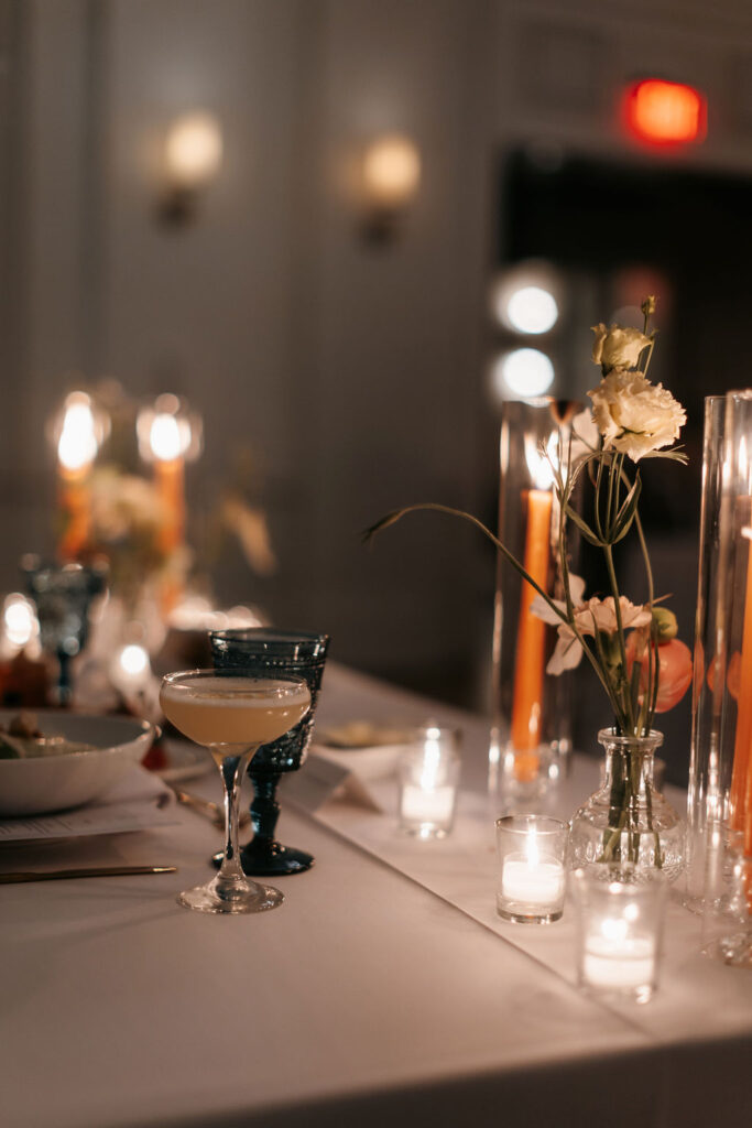 A candlelit table with the focus on a cocktail in a glass coupe