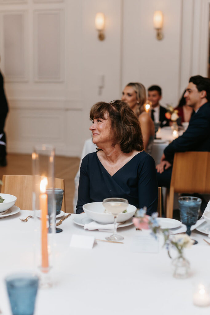 The mother of the bride smiling at her husband and daughter as they share a dance