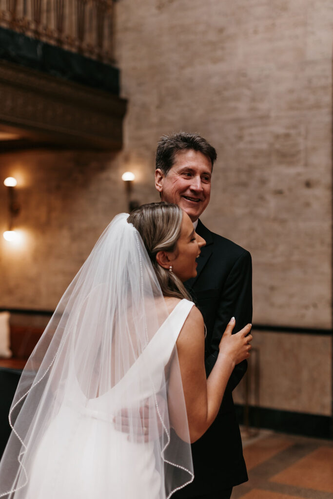 The bride and her father looking off to the side and laughing at bystanders as they share a sweet moment