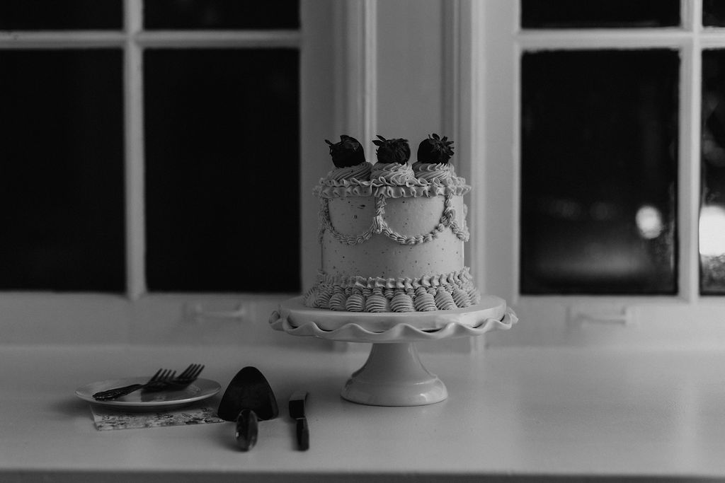 A white cake with piping and chocolate covered strawberries atop a cake stand 