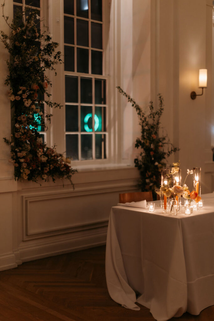 Wedding reception tables with orange taper candles and orange flowers in evening light