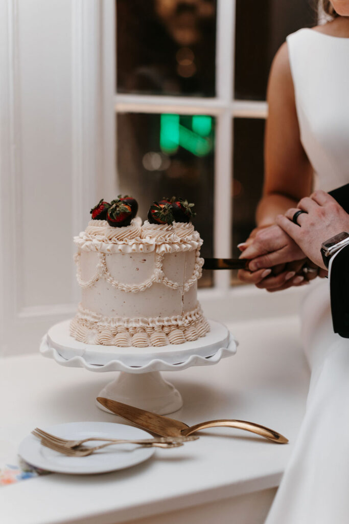 A white cake with piping and chocolate covered strawberries atop a cake stand 