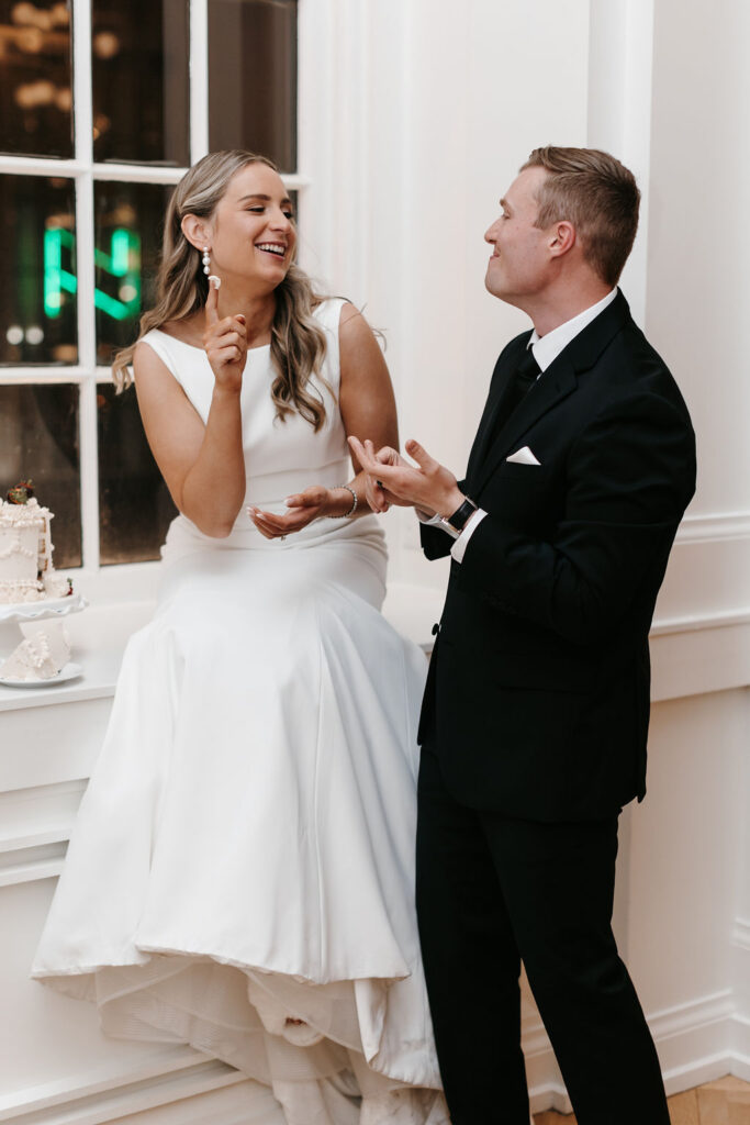 A bride and groom laugh at each other during the wedding cake cutting