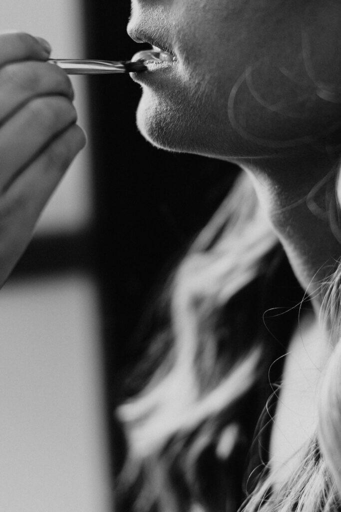 Black and white image of a woman applying lipstick with a brush