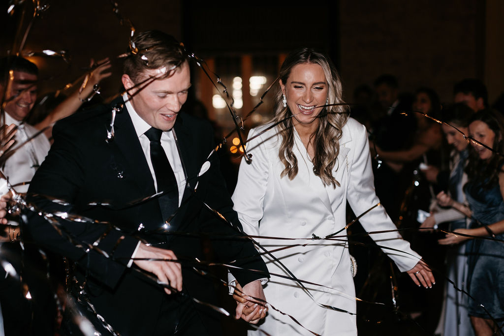 A bride and groom laugh during a send off with silver streamers