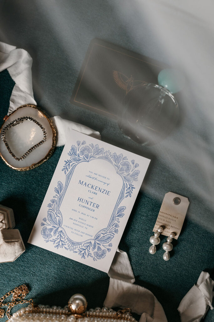 Blue wedding invitations surrounded by bridal accessories including diamond bracelet, pearl earrings, and wedding veil