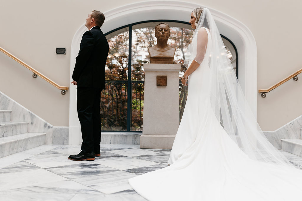 A groom stands with his back turned to the bride as she waits to reveal herself during a wedding first look