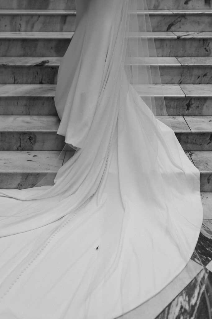 A sweeping photo of a wedding dress train and veil as it lays across a marble staircase