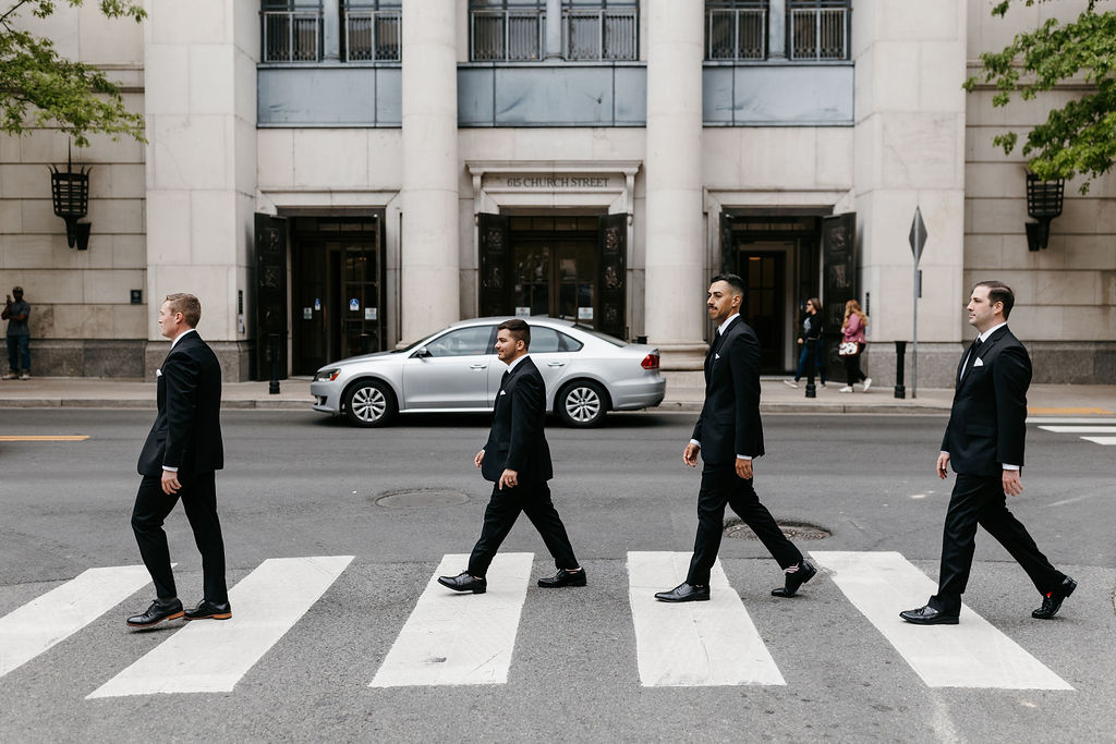 Groomsmen walk across a crosswalk in downtown Nashville while wearing black suits