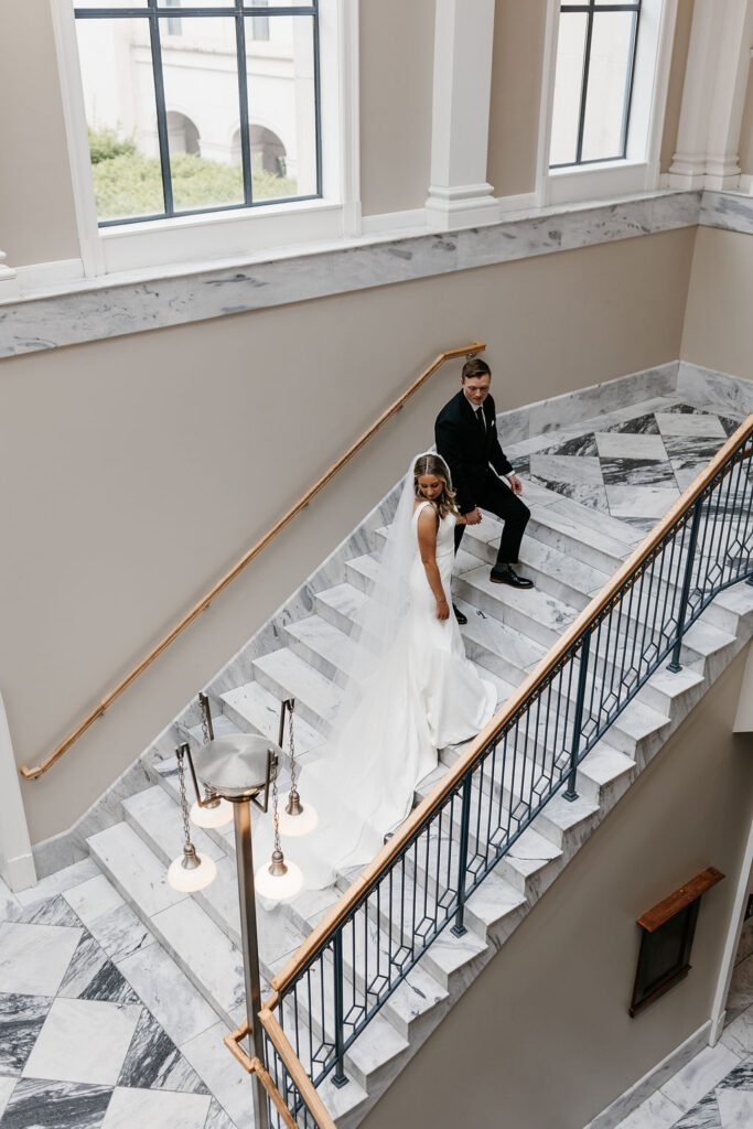 The bride and groom stand on a marble staircase in the light filled Nashville Public Library main branch