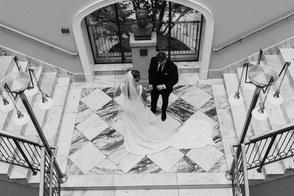 A bride and groom admire each other standing on a marble terrace with marble square tiles